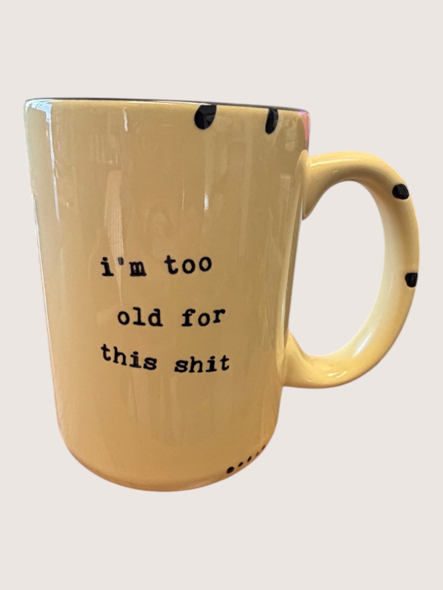 Yellow mug with black text 'i'm too old for this shit' on a light gray background