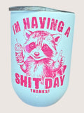 Light blue travel cup/tumbler with pink raccoon graphic and text on a light pink background