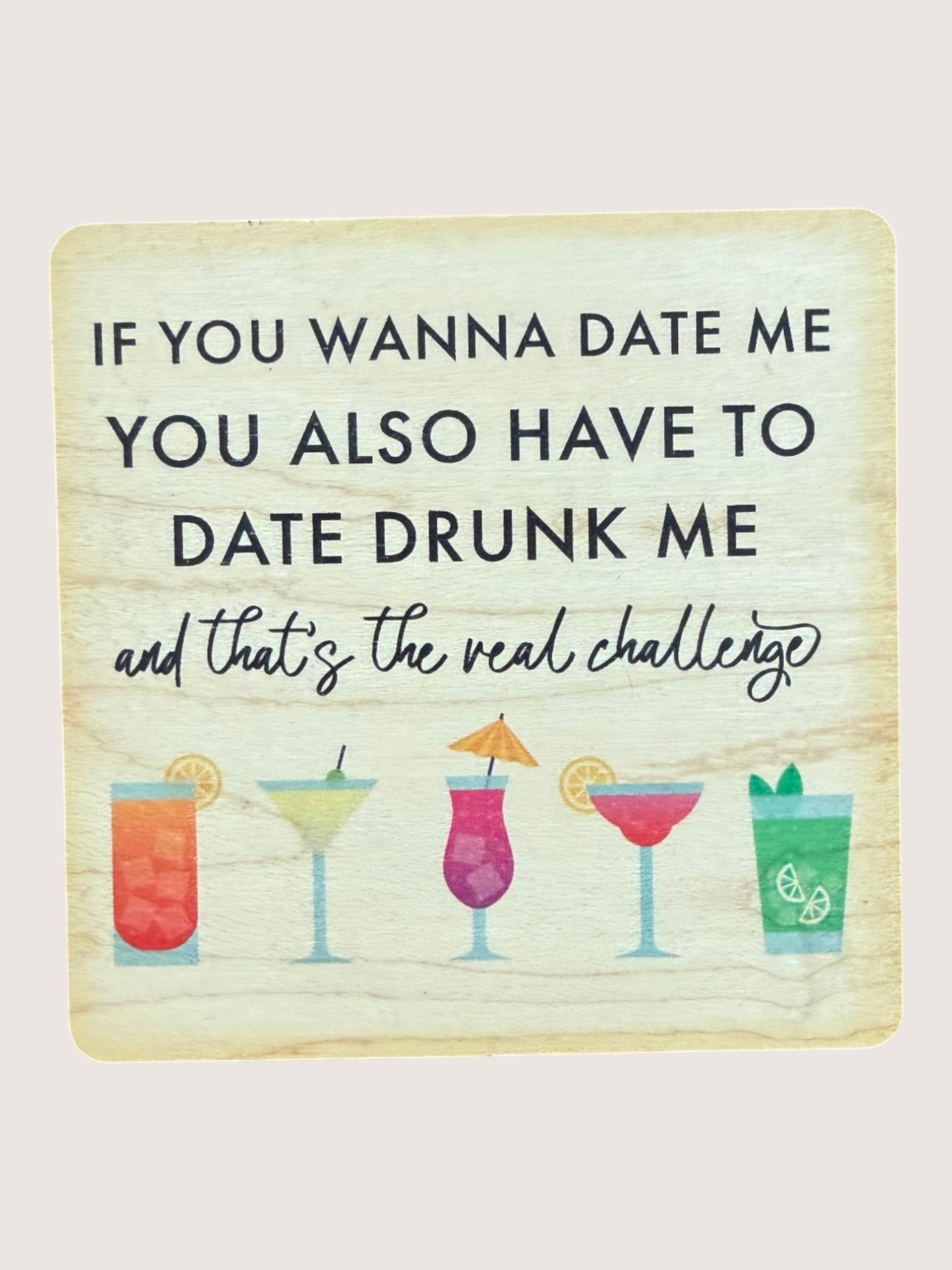 Wooden coaster with cocktail illustrations and humorous text on a light background
