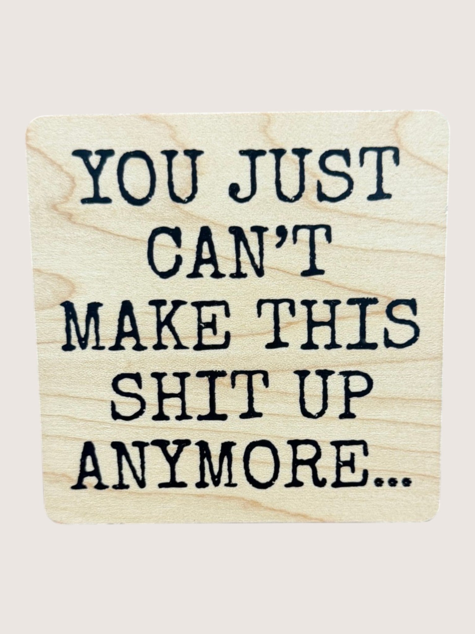 Wooden coaster with text 'YOU JUST CAN'T MAKE THIS SHIT UP ANYMORE...' on a light background