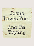 Wooden coaster with text 'Jesus Loves You... And I'm Trying' on a light background