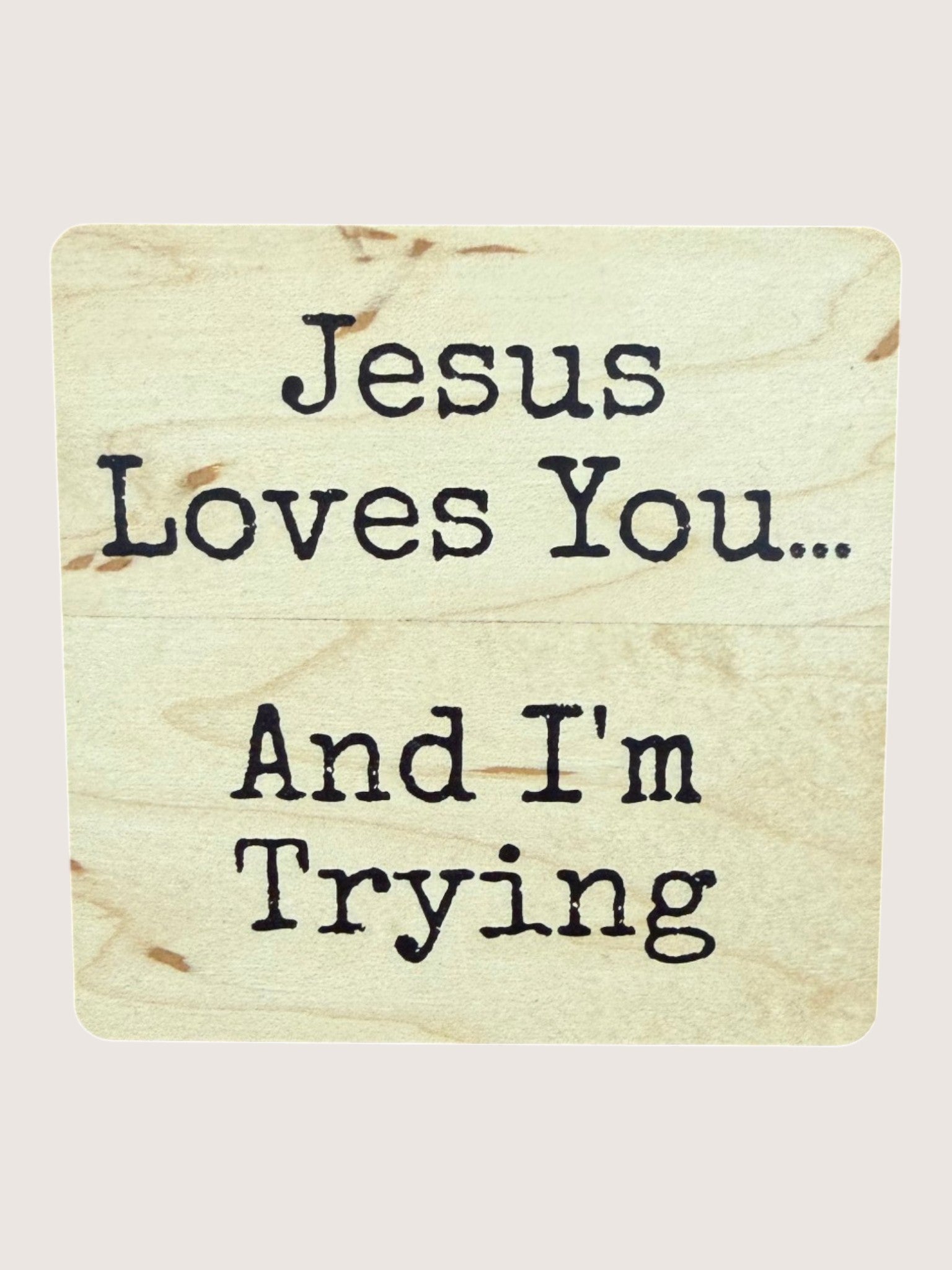 Wooden coaster with text 'Jesus Loves You... And I'm Trying' on a light background