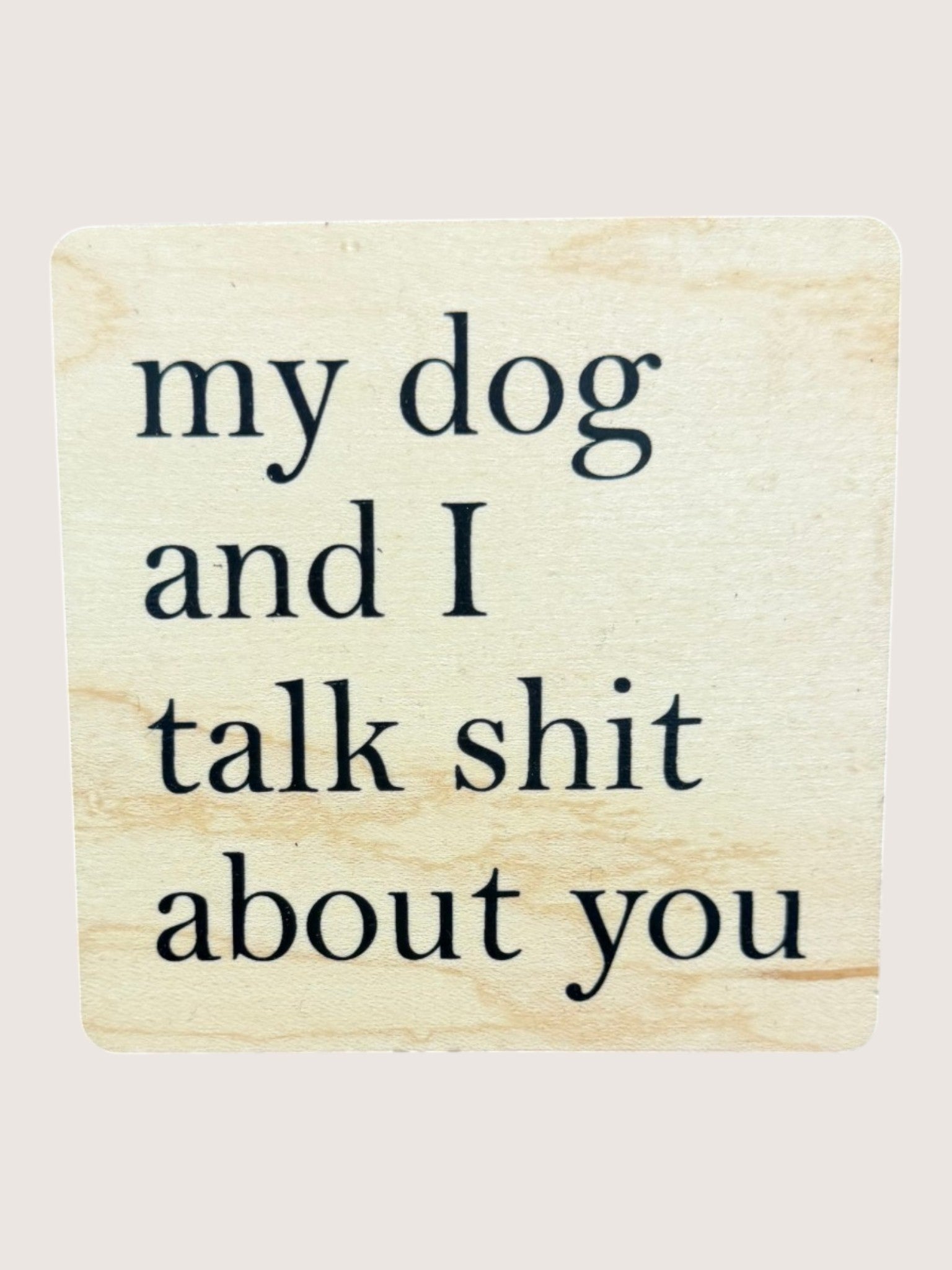 Wooden coaster with text 'my dog and I talk shit about you' on a beige background