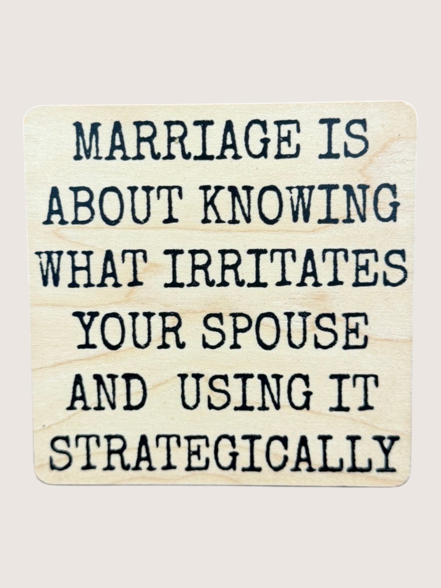 Wooden coaster with humorous quote about marriage on a light background