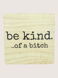 Wooden coaster with 'be kind...of a bitch' text on a light background