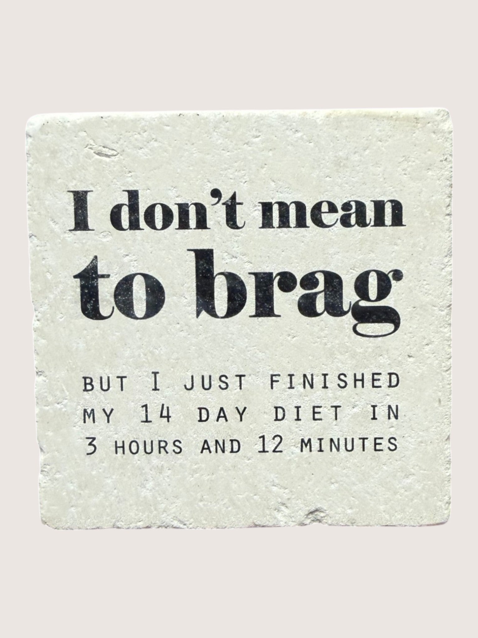 coaster with Text on a stone surface saying 'I don't mean to brag but I just finished my 14 day diet in 3 hours and 12 minutes'.