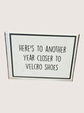 Card with text 'Here's to another year closer to velcro shoes' on a white background