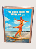 Card with a vintage-style illustration of two people water skiing, text 'This card made me think of us' on a blue background.