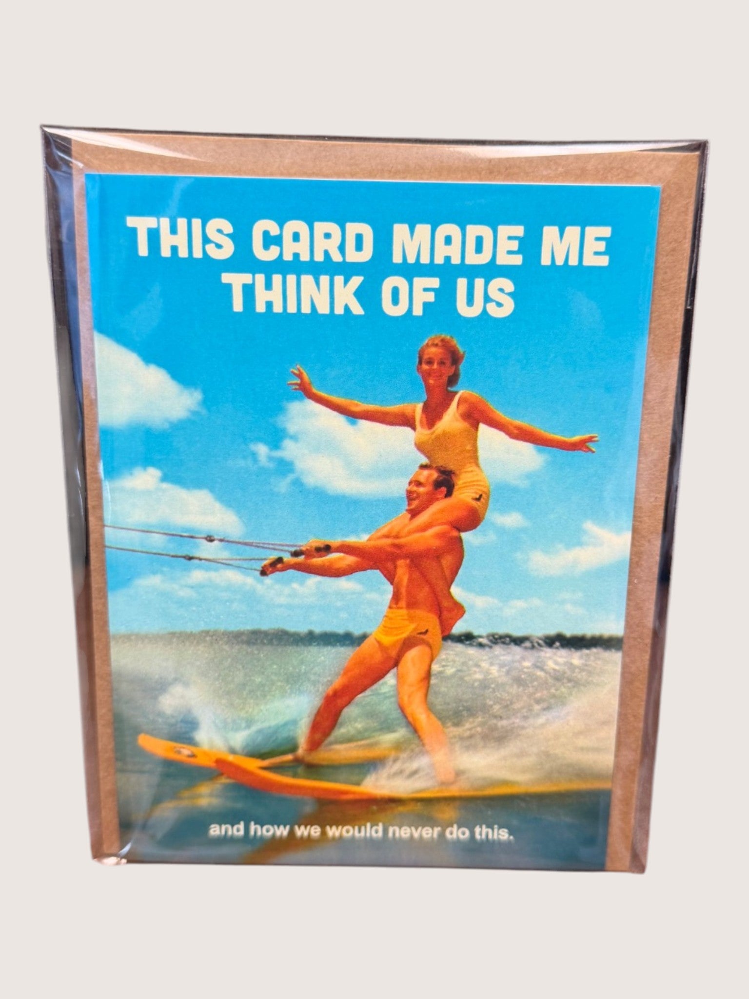 Card with a vintage-style illustration of two people water skiing, text 'This card made me think of us' on a blue background.