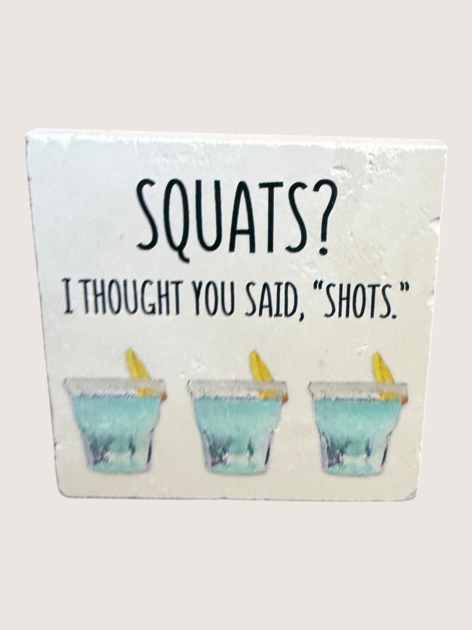 coaster with 'SQUATS? I Thought You Said, 'Shots.'' text and shot glass illustrations.