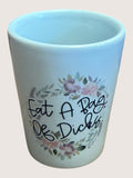 White Ceramic shot glass with floral design and text on a plain background