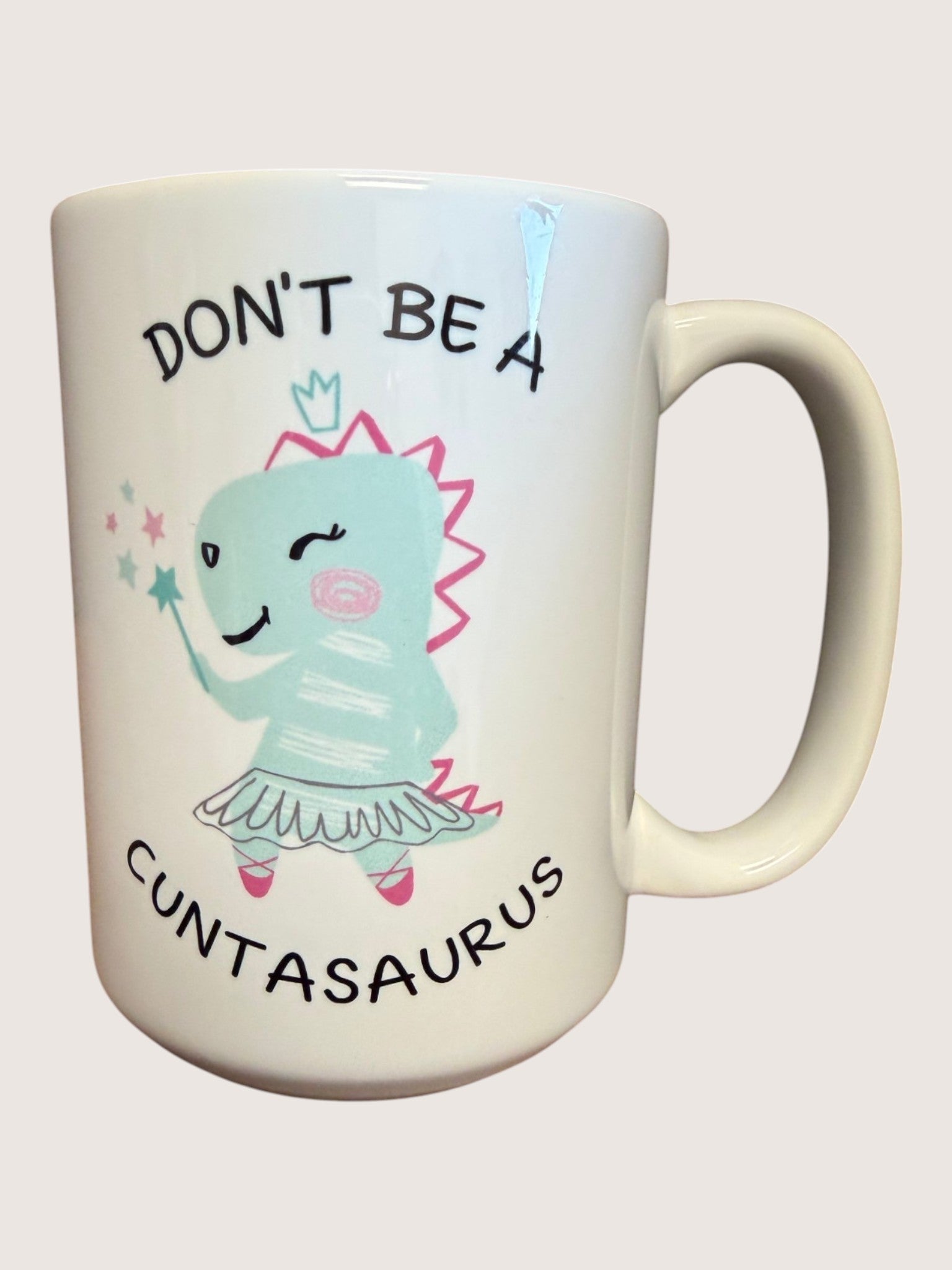 Mug with cartoon character and text 'Don't be a Cuntasaurus' on a light background