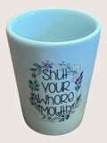 Light blue ceramic shot glass with floral design and text on a beige background