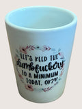 White shot glass with floral design and text on a light pink background