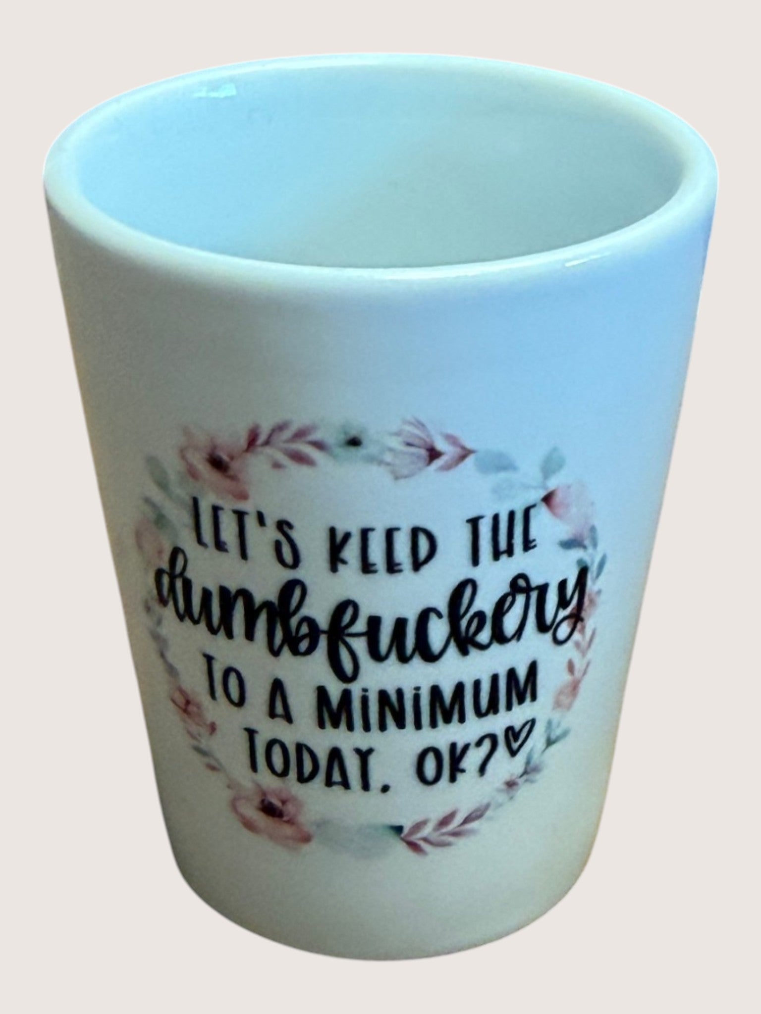 White shot glass with floral design and text on a light pink background