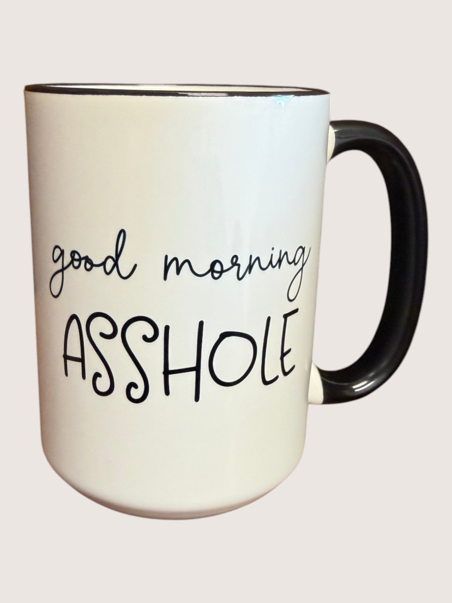 White mug with black text 'good morning ASSHOLE' on a light pink background