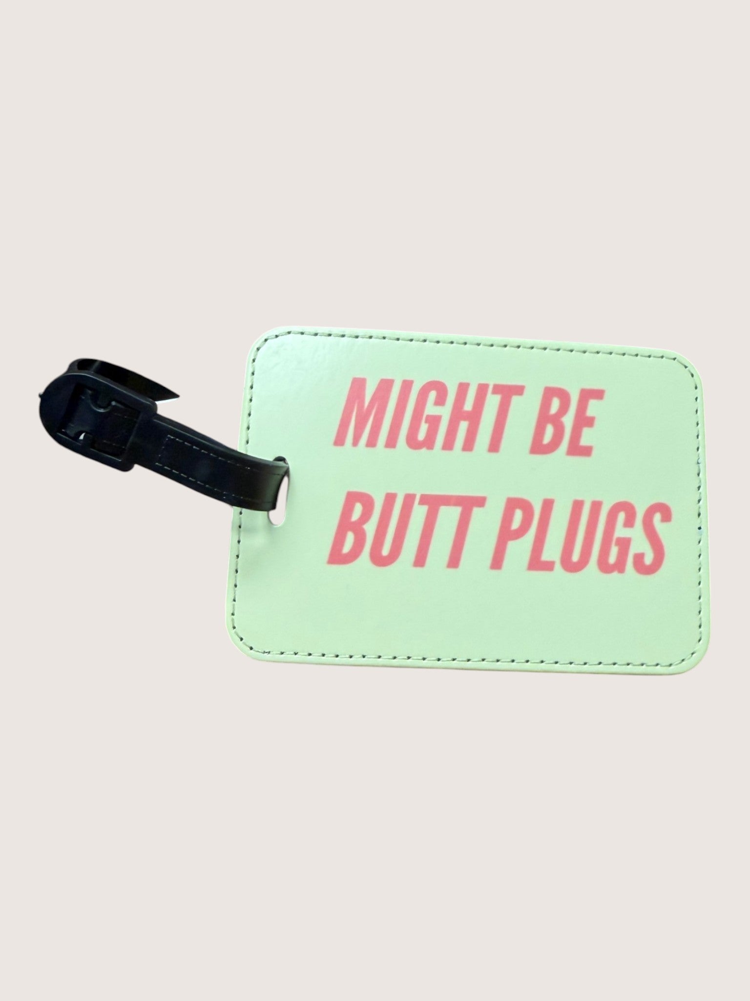 Light green luggage tag with pink text 'MIGHT BE BUTT PLUGS' on a beige background