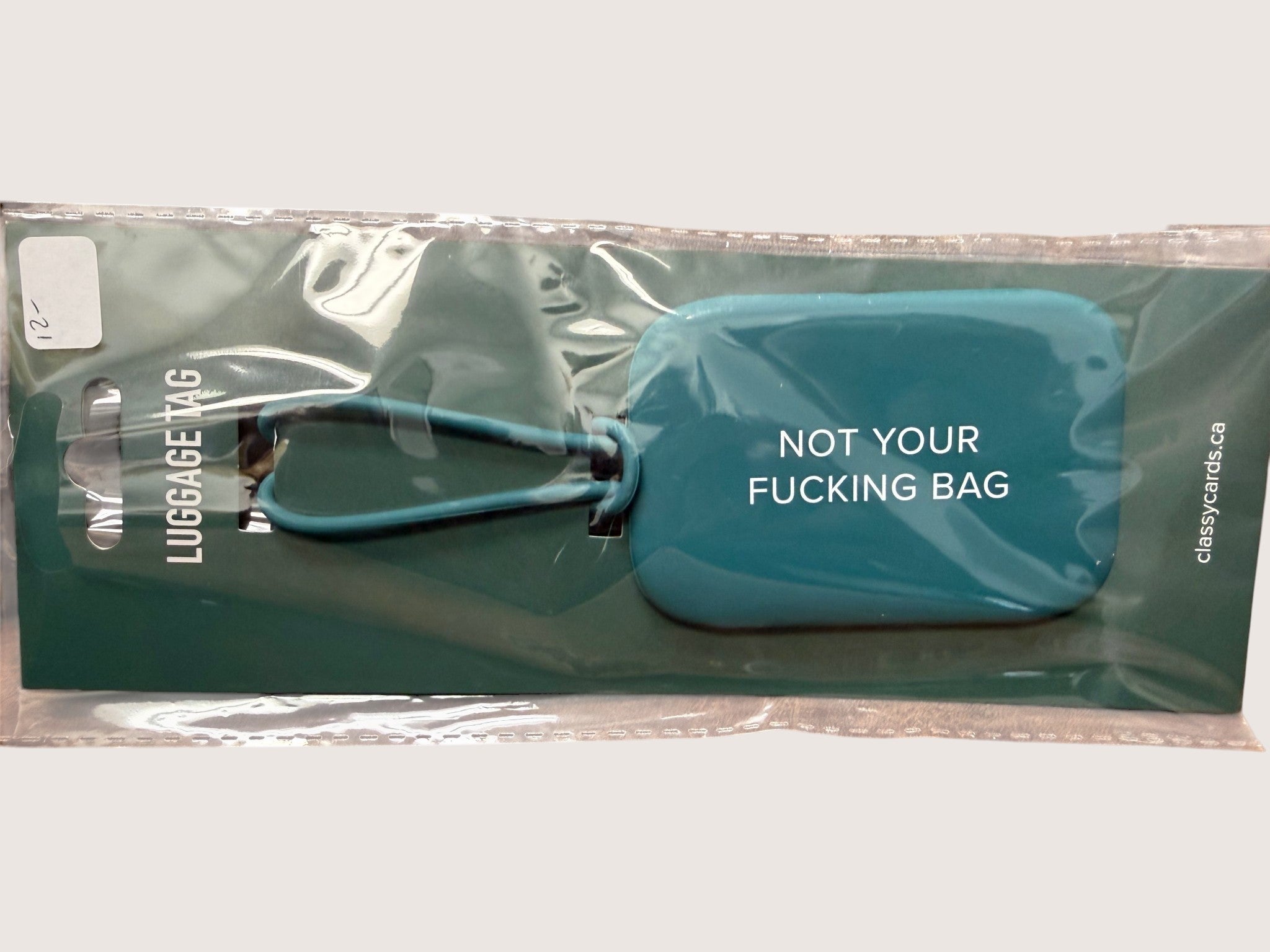 Teal luggage tag with text 'Not Your Fucking Bag' in clear packaging
