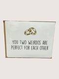 Card with two interlocking rings and text 'You two weirdos are perfect for each other' on a white background