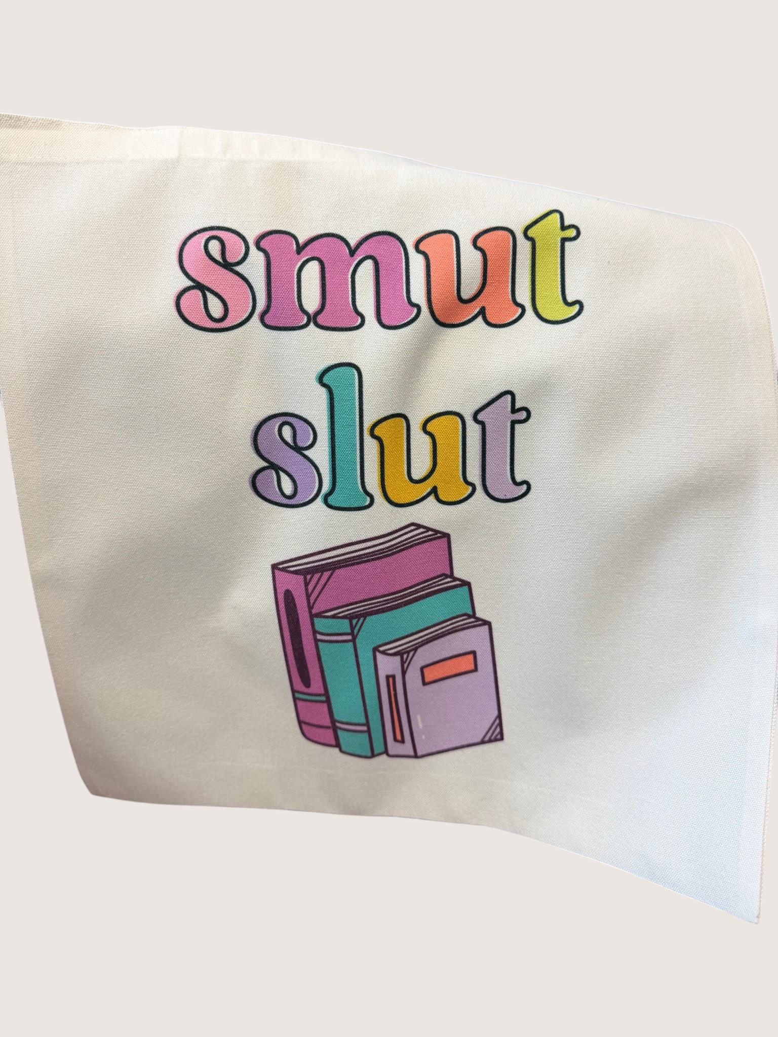 Tote bag with colorful text 'smut slut' and book illustrations on a white background