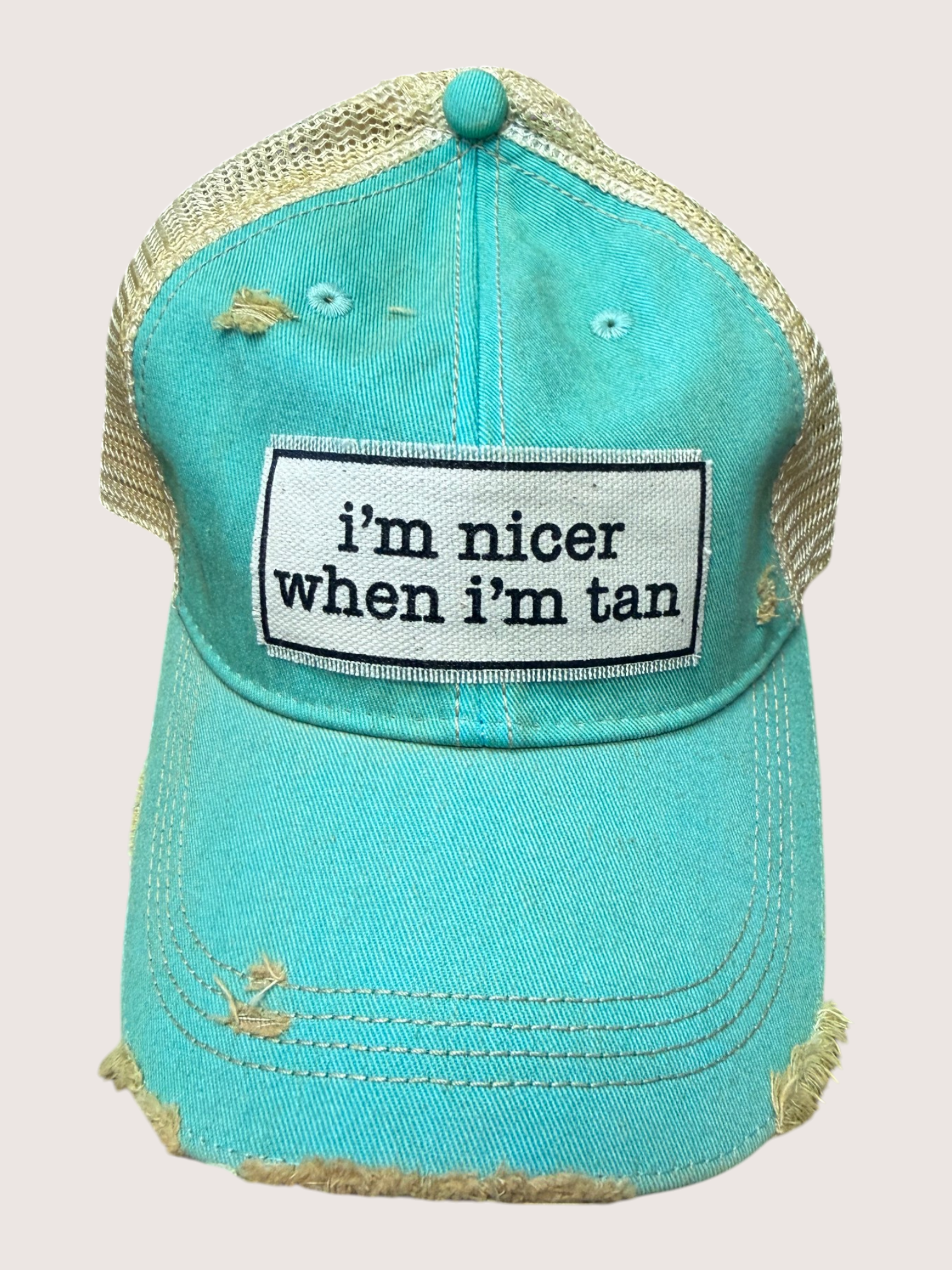 Turquoise cap with 'i'm nicer when i'm tan' patch on a light pink background