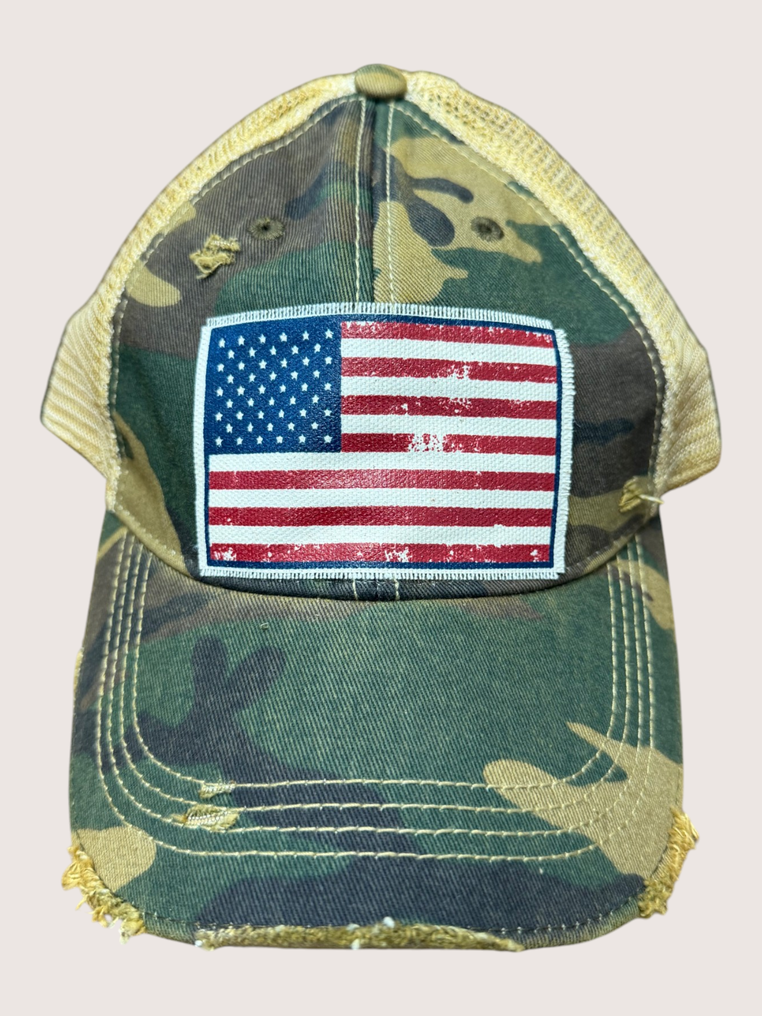Camouflage cap with American flag patch on a light pink background