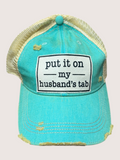 Turquoise cap with text 'put it on my husband's tab' on a light gray background