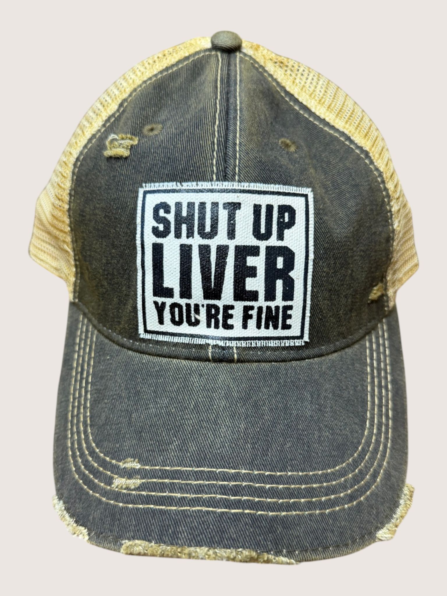 Black and yellow cap with 'Shut Up Liver You're Fine' text on a beige background