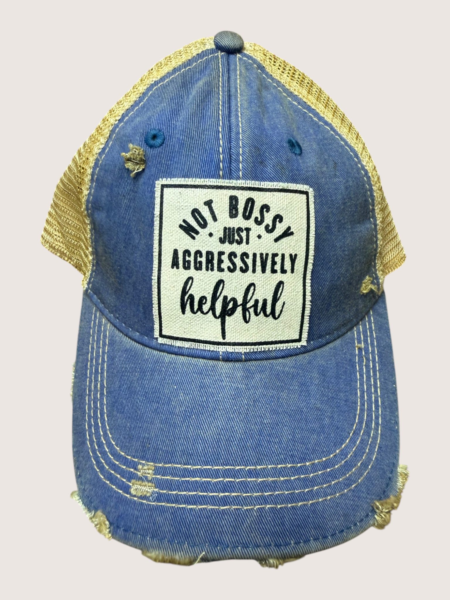 Blue denim cap with yellow mesh back and text patch on a light pink background