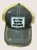 Black and yellow cap with 'Welcome to the Shitshow' patch on a light gray background