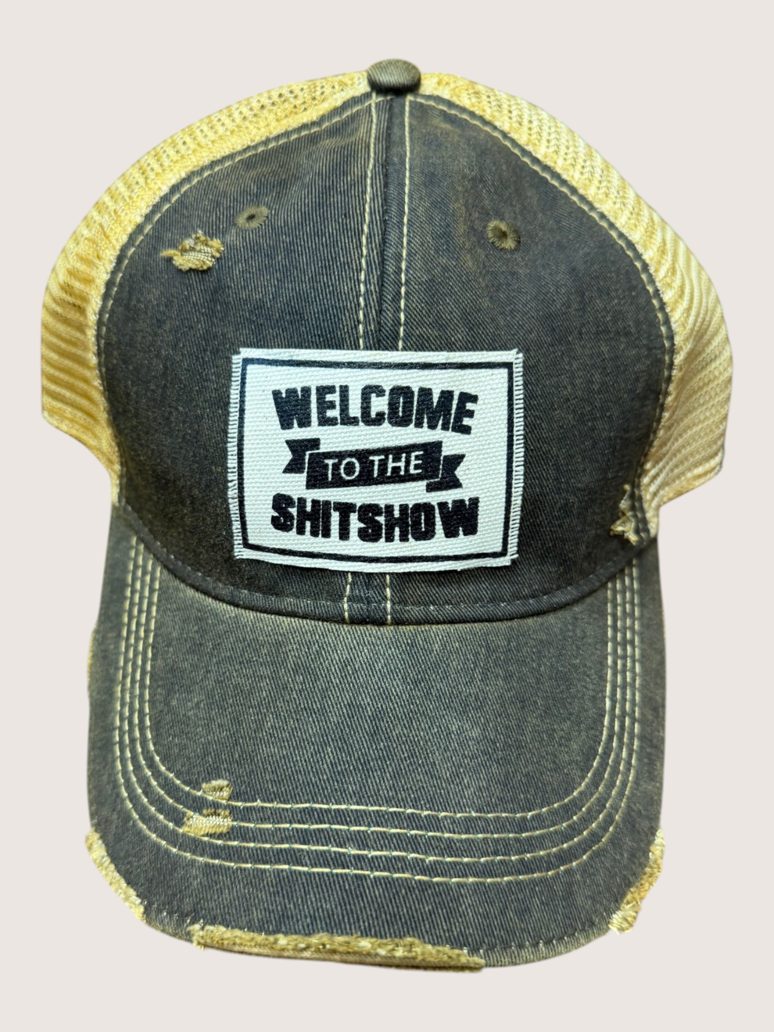 Black and yellow cap with 'Welcome to the Shitshow' patch on a light gray background