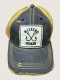 Blue trucker cap with 'Weekend Hooker' patch on a beige background