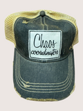 Distressed denim cap with 'Chaos coordinator' patch on a light pink background