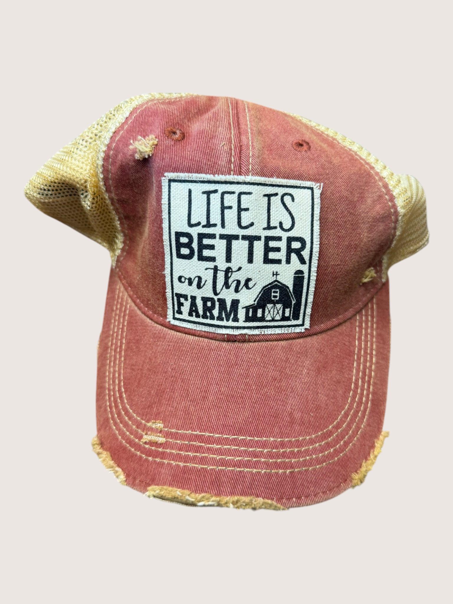 Red distressed cap with 'Life is Better on the Farm' patch on a light gray background