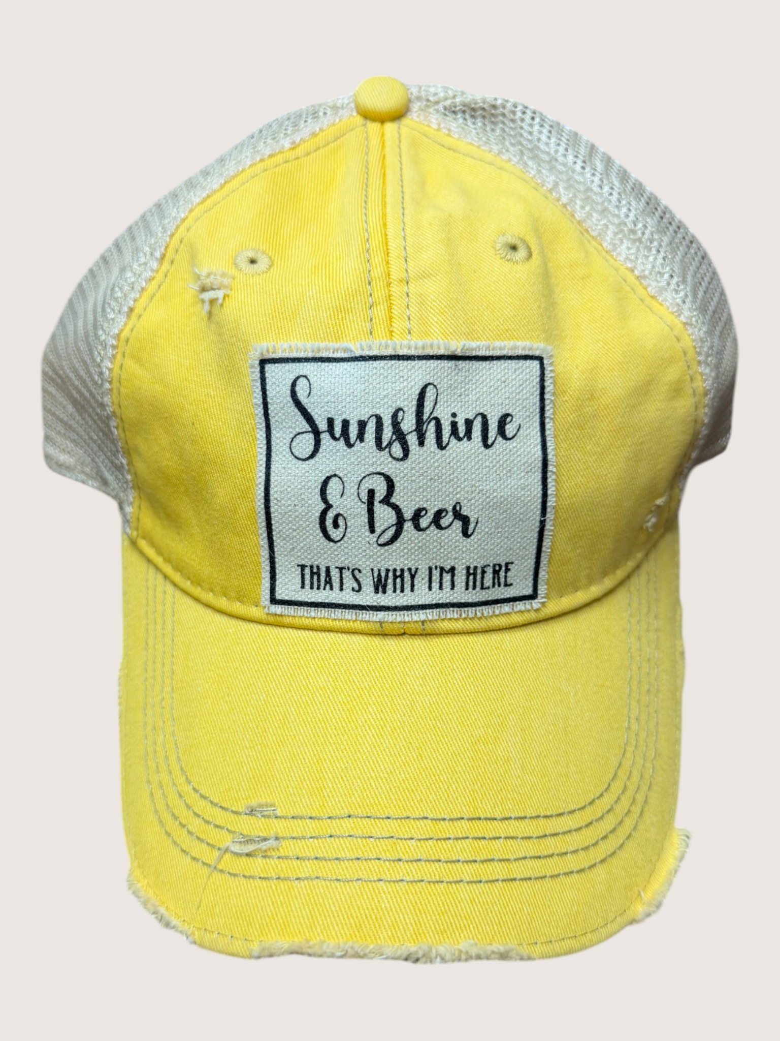Yellow cap with 'Sunshine & Beer, That's Why I'm Here' patch on a light pink background