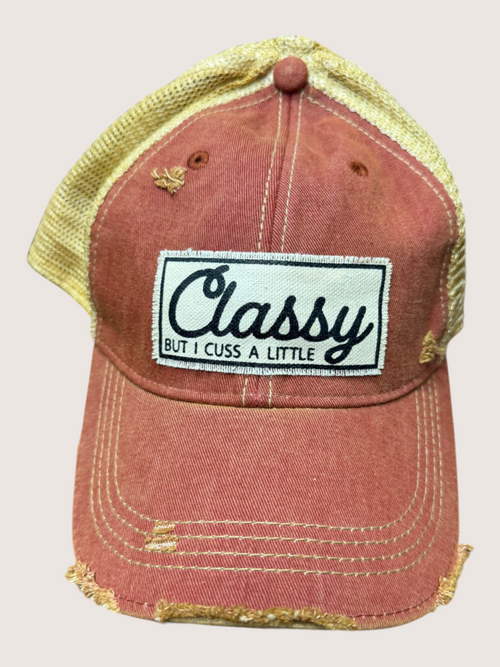 Red distressed cap with 'Classy But I Cuss A Little' patch on a beige background
