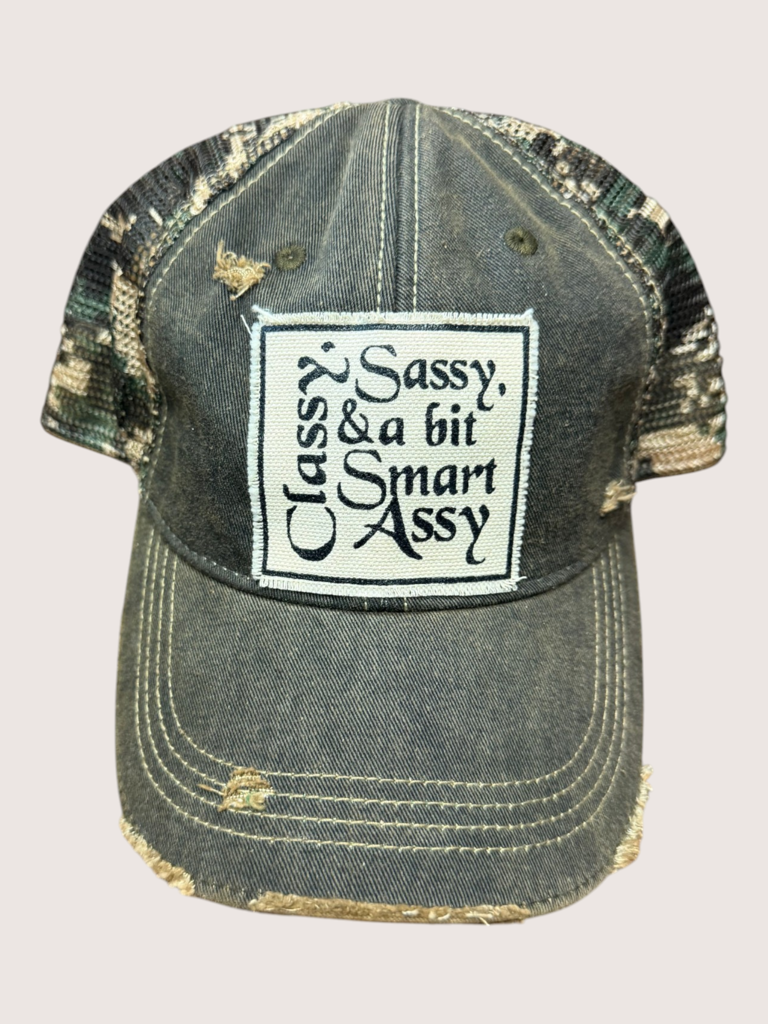 Vintage-style cap with a patch reading 'Sassy, Classy & a bit Smart Assy' on a light gray background