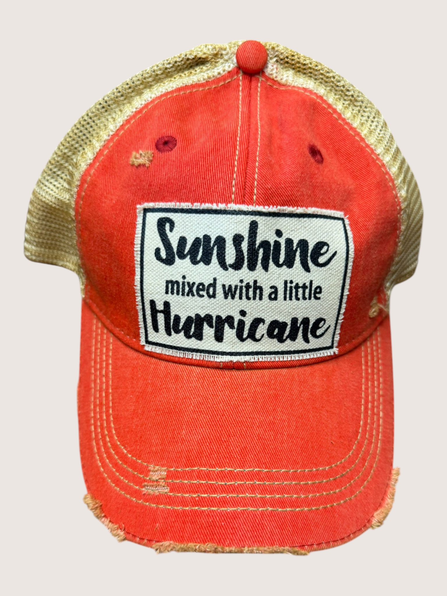 Red cap with gold brim and 'Sunshine mixed with a little Hurricane' text on a light gray background