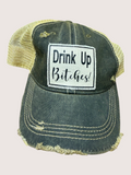 Vintage-style cap with 'Drink Up Bitches!' patch on a light pink background