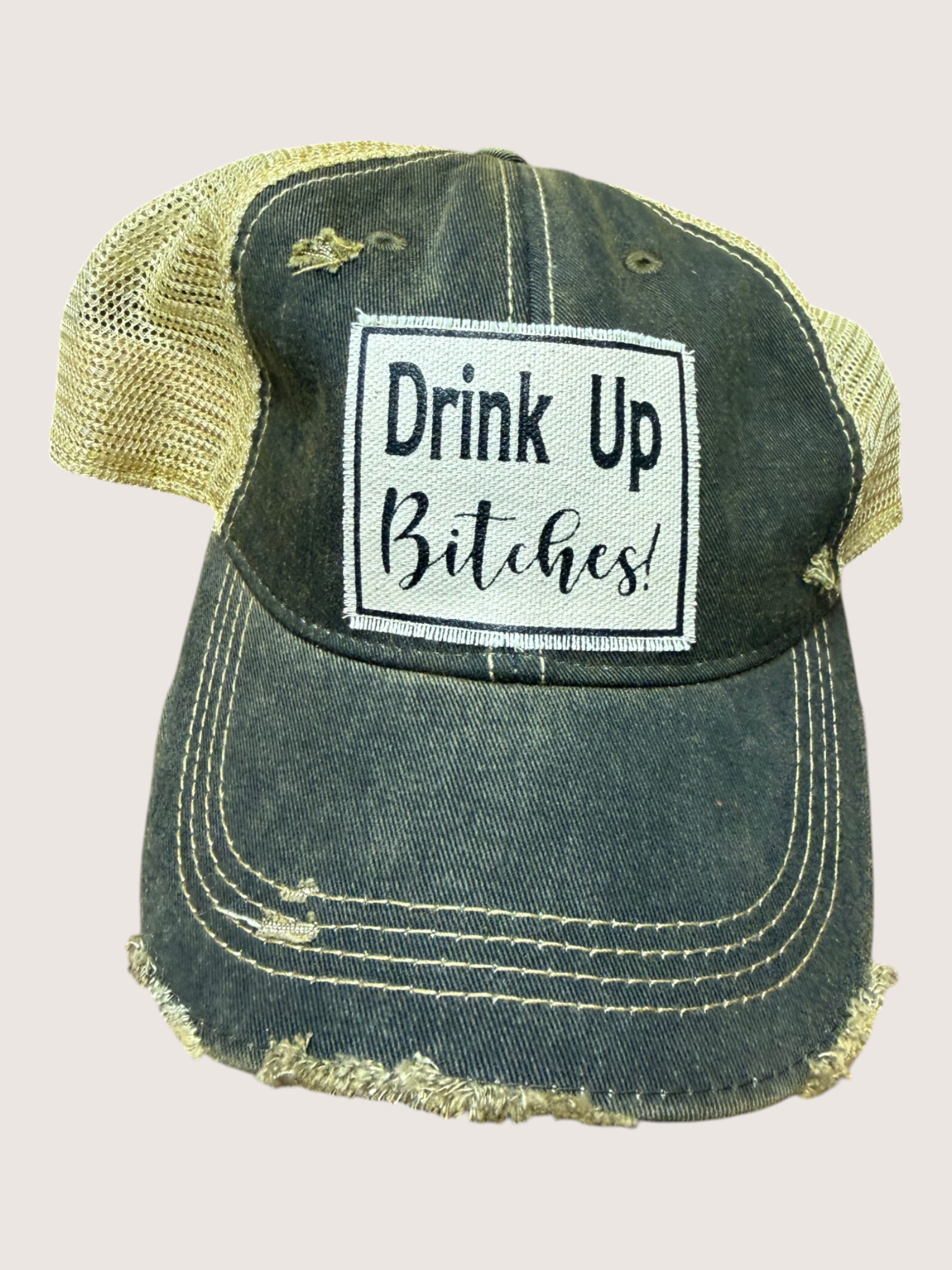 Vintage-style cap with 'Drink Up Bitches!' patch on a light pink background