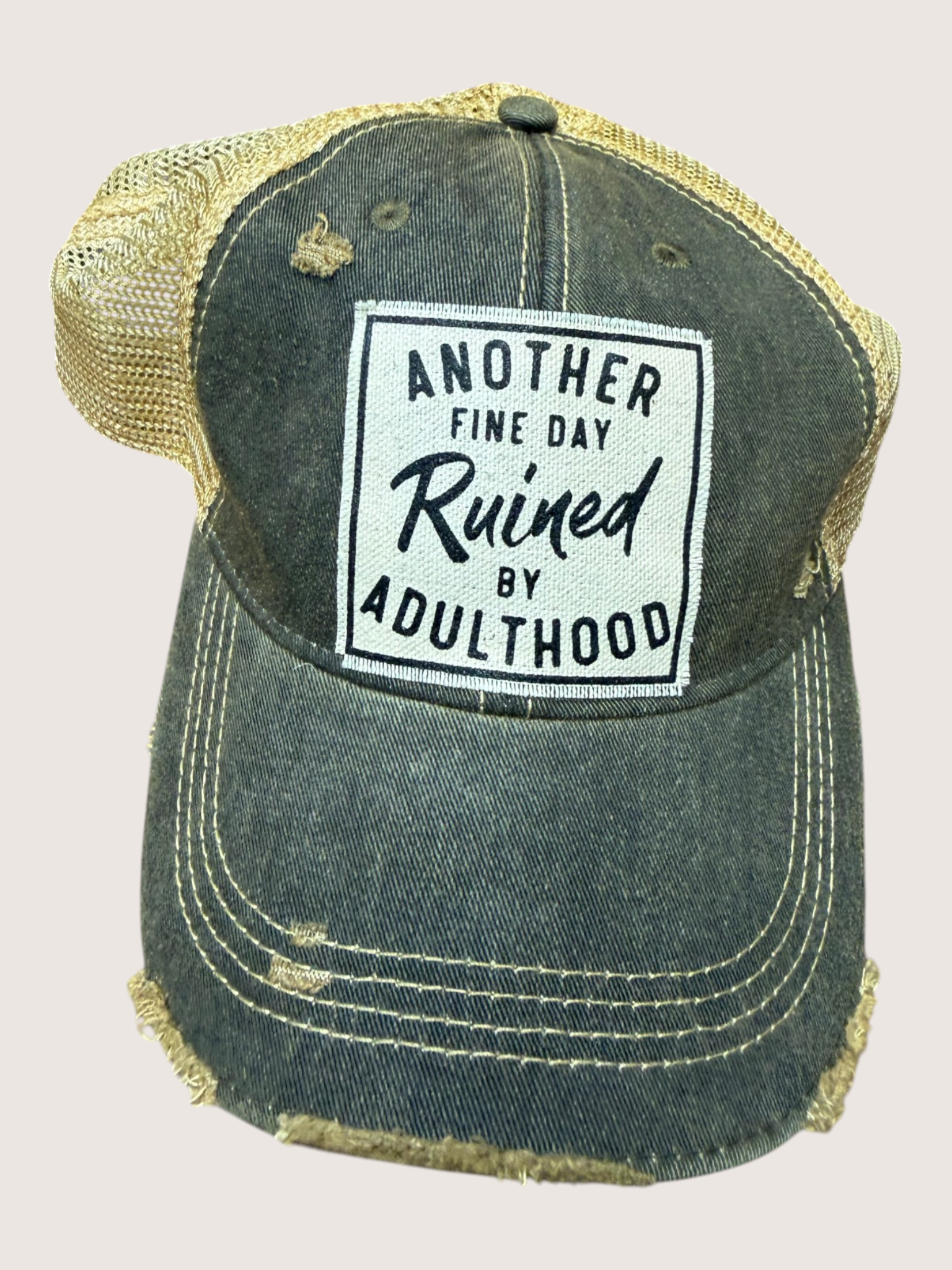 Distressed denim cap with gold mesh back and humorous patch on a light gray background