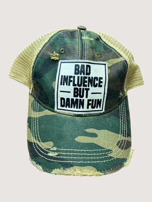 Camouflage baseball cap with a patch saying 'Bad Influence But Damn Fun' on a light gray background