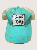 Turquoise cap with 'Tanned & Tipsy' text on a beige background
