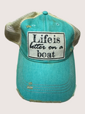 Turquoise cap with 'Life is better on a boat' patch on a light gray background