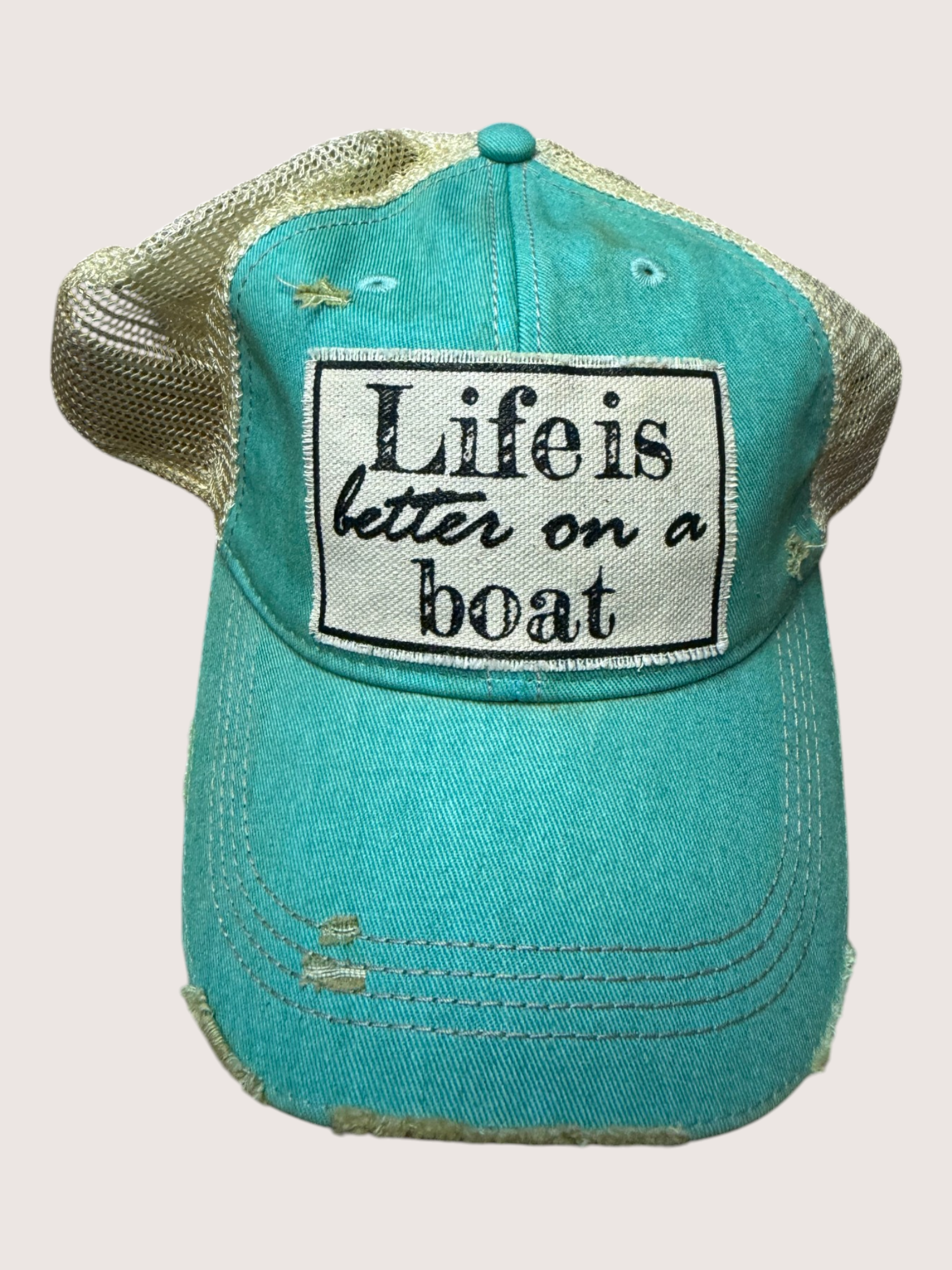 Turquoise cap with 'Life is better on a boat' patch on a light gray background