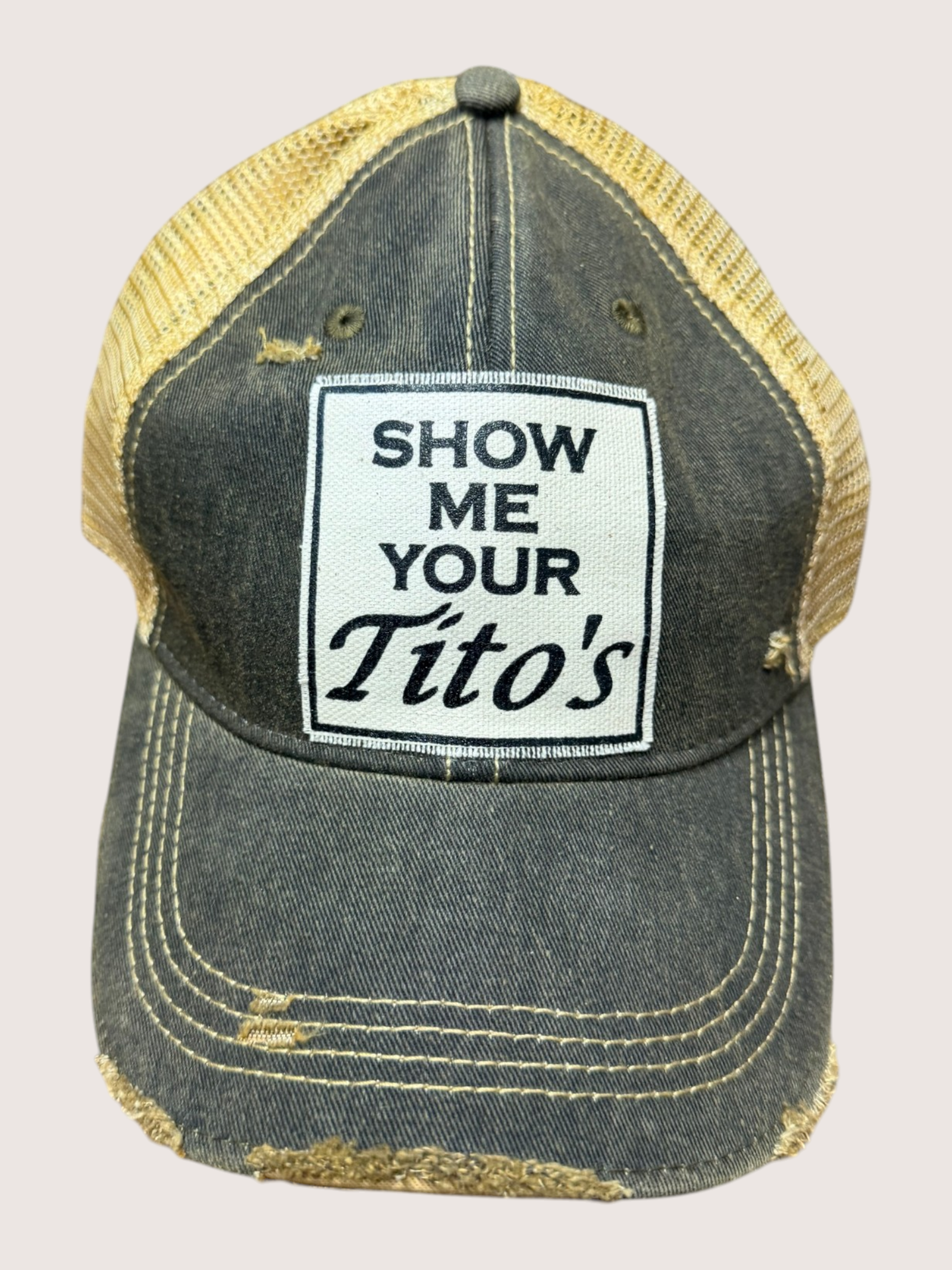 Vintage-style cap with 'Show Me Your Tito's' patch on a light gray background