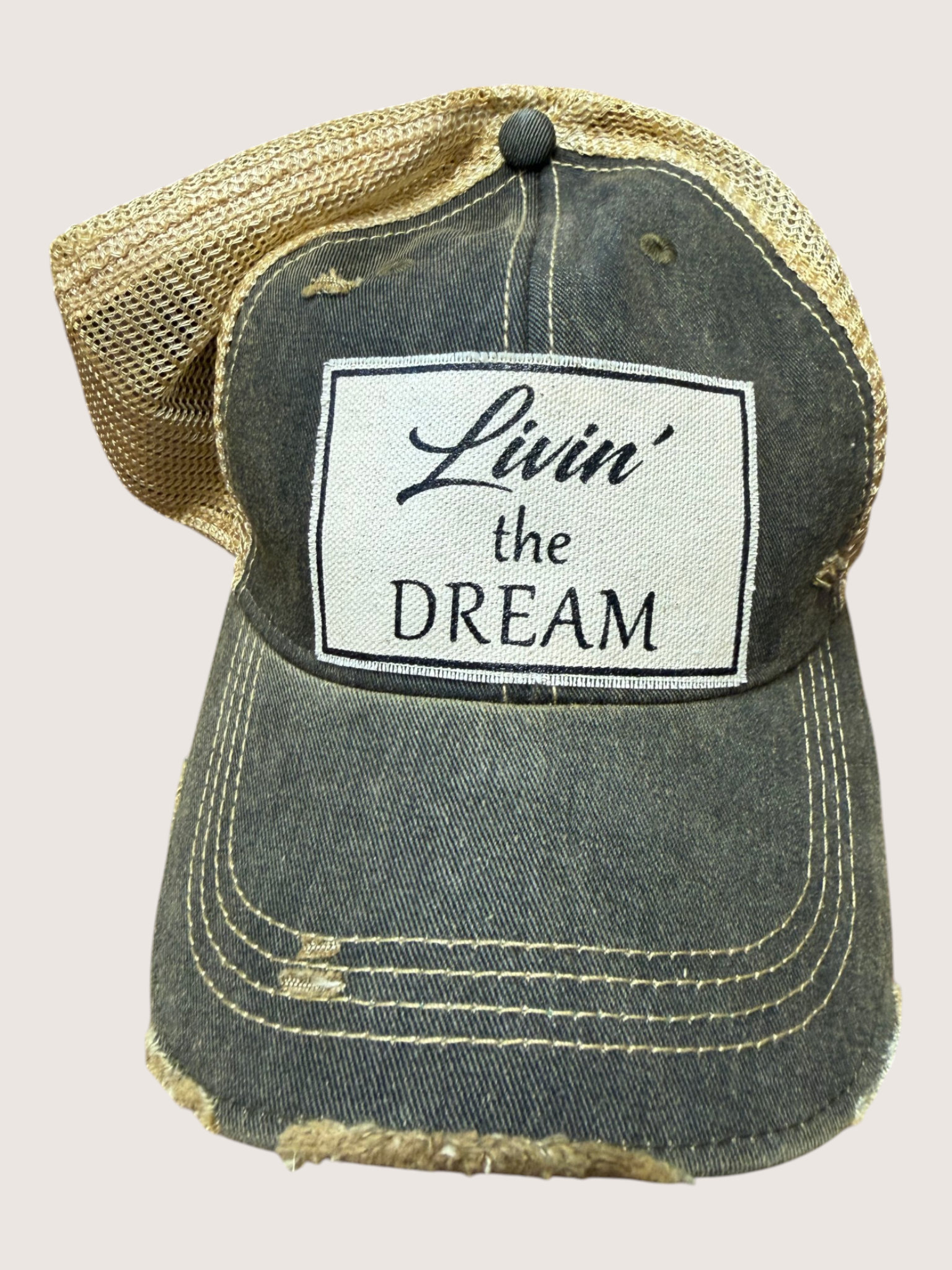 Distressed denim cap with 'Livin' the Dream' patch on a light pink background