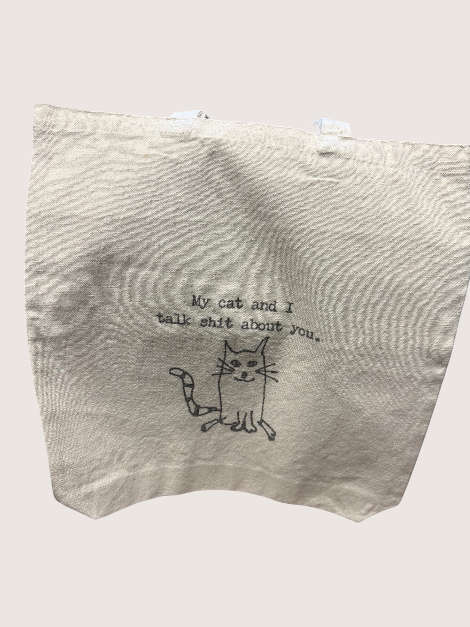 Beige tote bag with a cat illustration and text on a white background