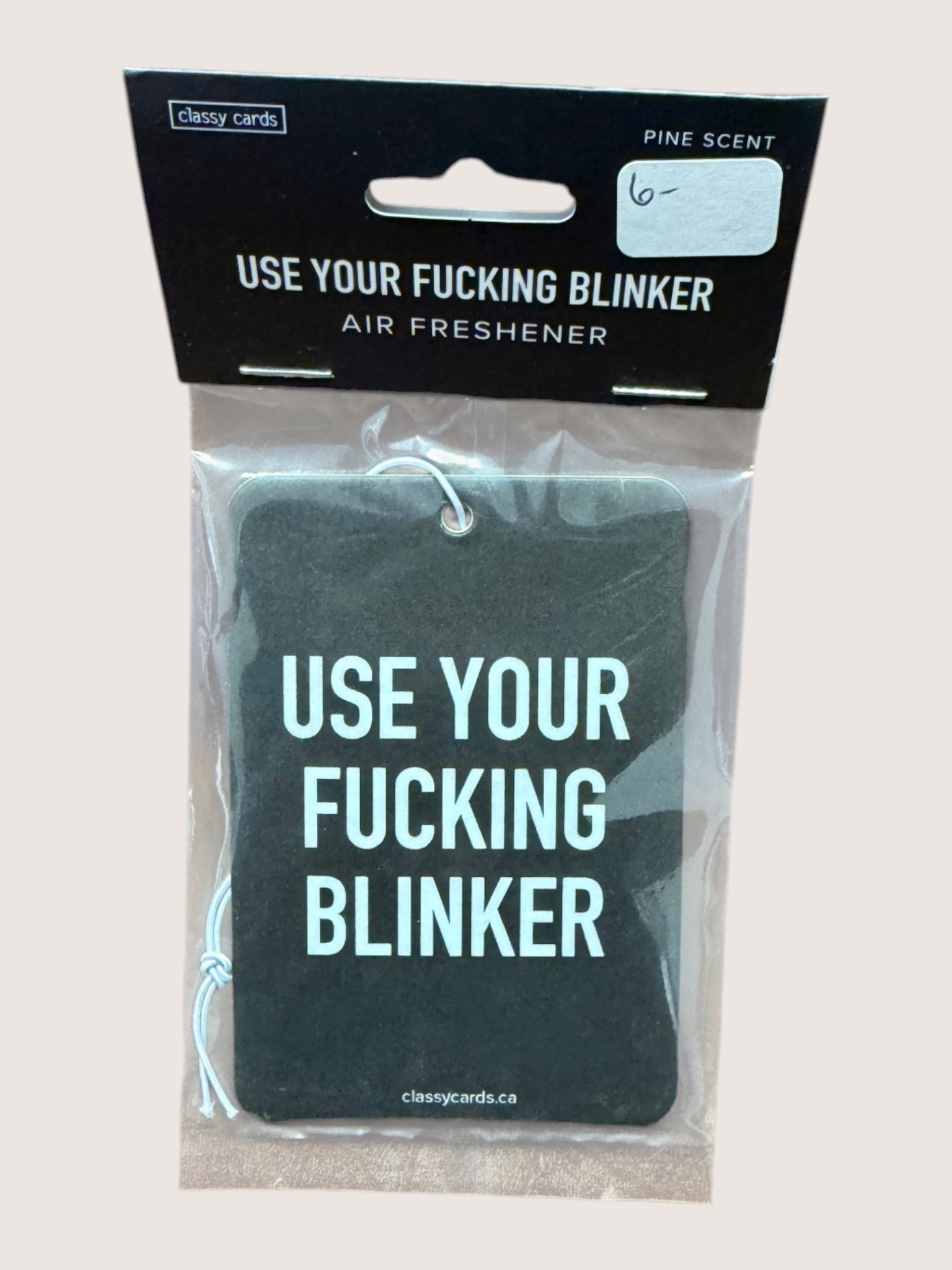 Air freshener with text 'Use Your Fucking Blinker' in packaging on a light gray background