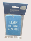 Blue air freshener with text 'LEARN TO DRIVE ASSHOLE' in packaging on a light gray background